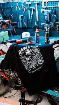 Camiseta RAW CUTS colgada en una moto dentro del taller