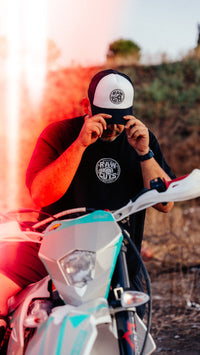 Modelo llevando la camiseta RAW CUTS junto a una moto custom, al atardecer